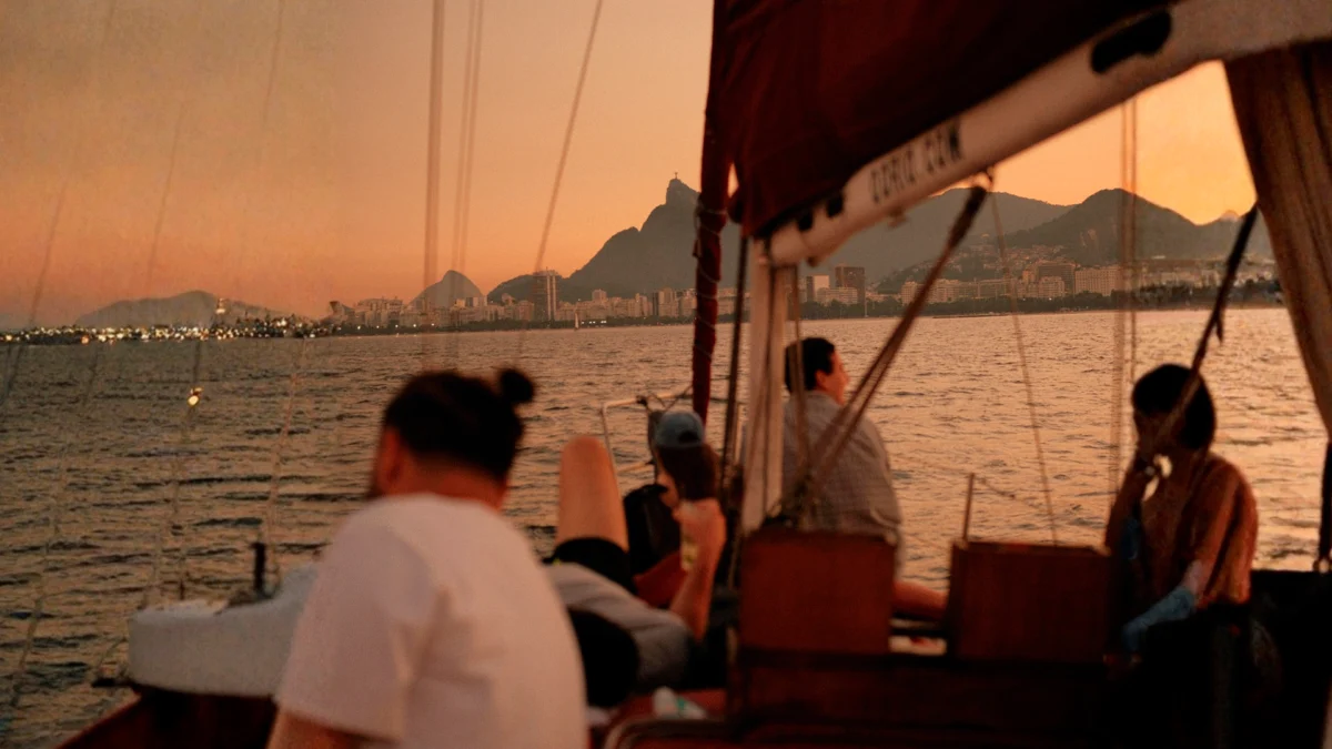 pessoas relaxam em um passeio de barco ao entardecer, navegando pelo mar com a vista icônica do morro do Corcovado e do Cristo Redentor no horizonte do Rio de Janeiro