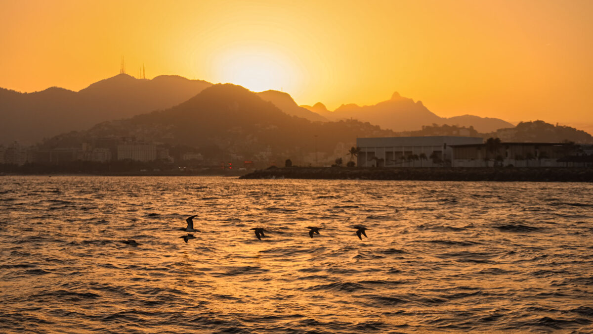 Pôr do sol sobre o Rio de Janeiro, com o mar em primeiro plano e as montanhas da cidade ao fundo