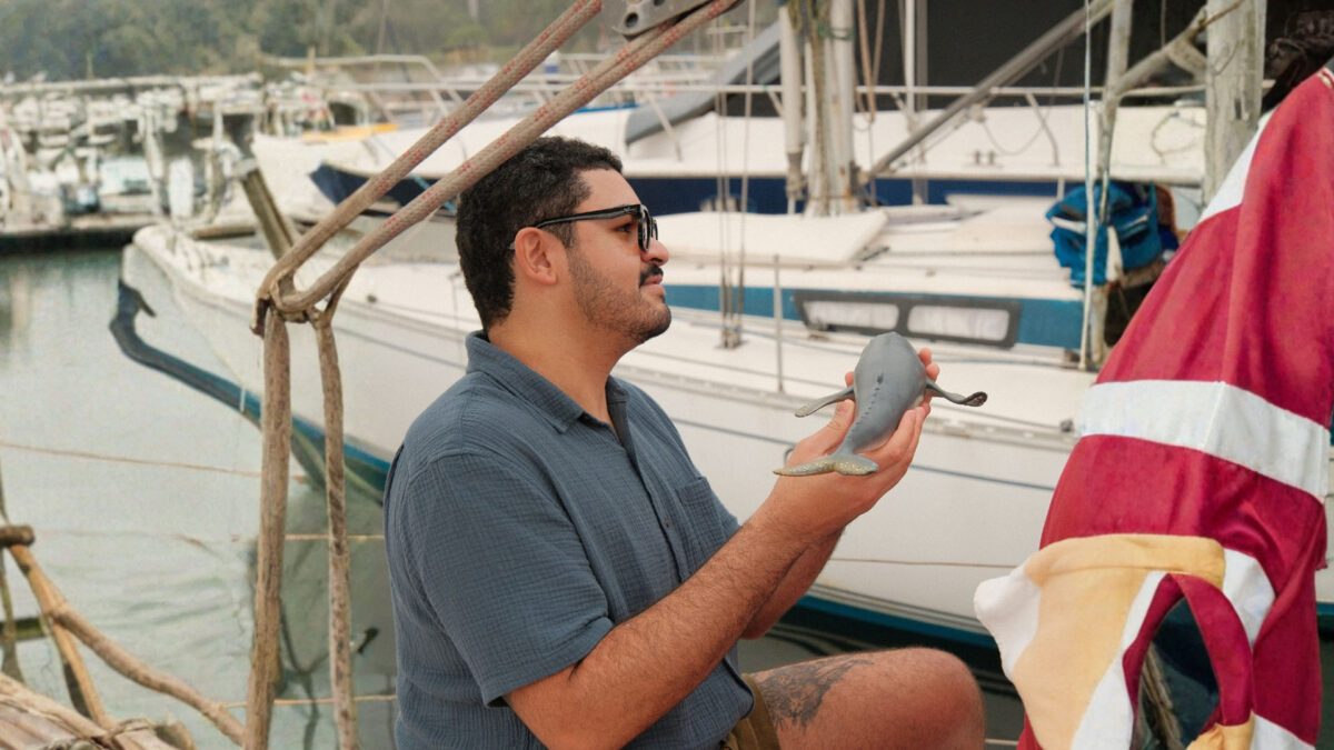 Homem de pele morena, cabelos curtos e óculos de sol, segurando uma pequena arraia a bordo de um passeio de barco da DDRio